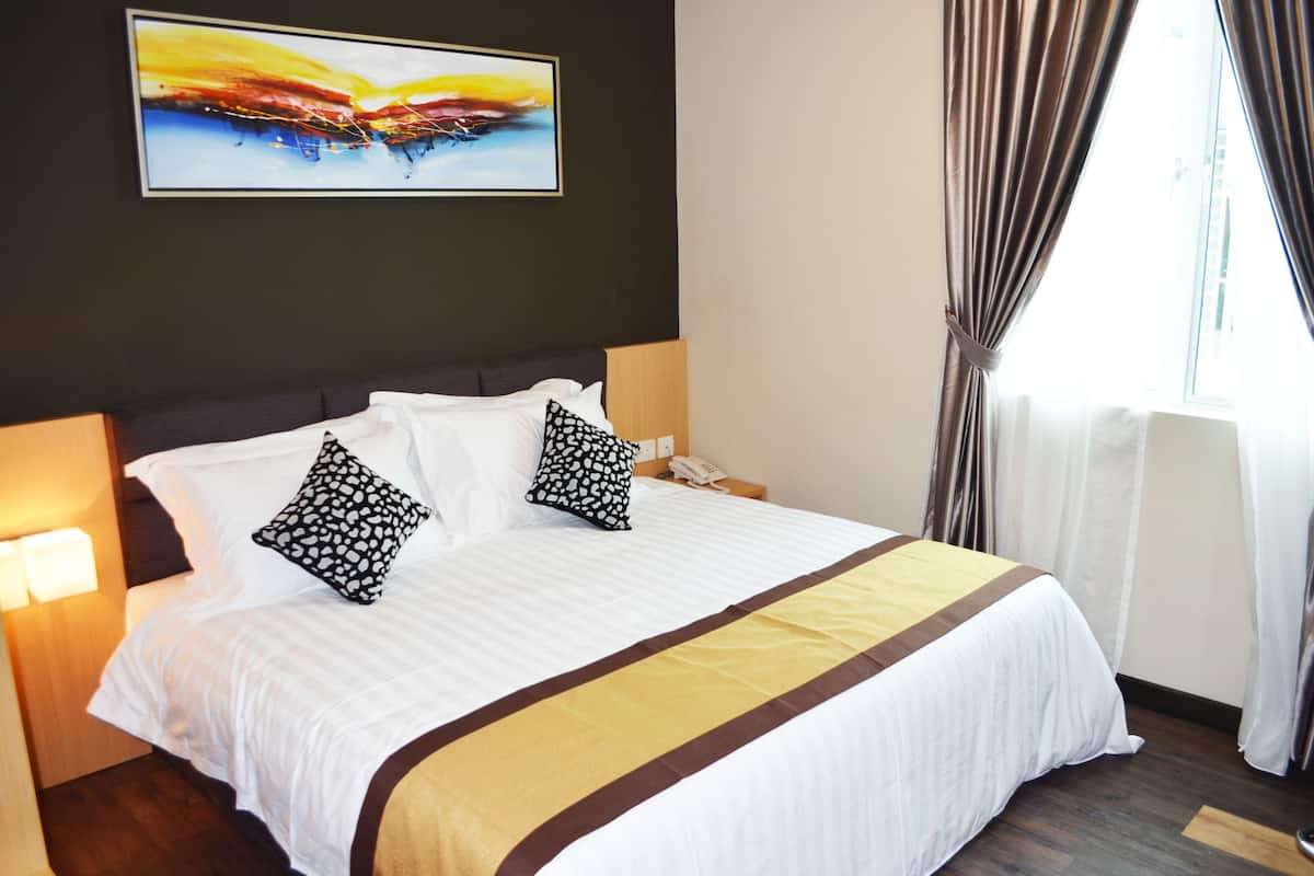 A hotel room with a large bed, two pillows, a bedside table with a phone, a painting on the wall, and a window with curtains.