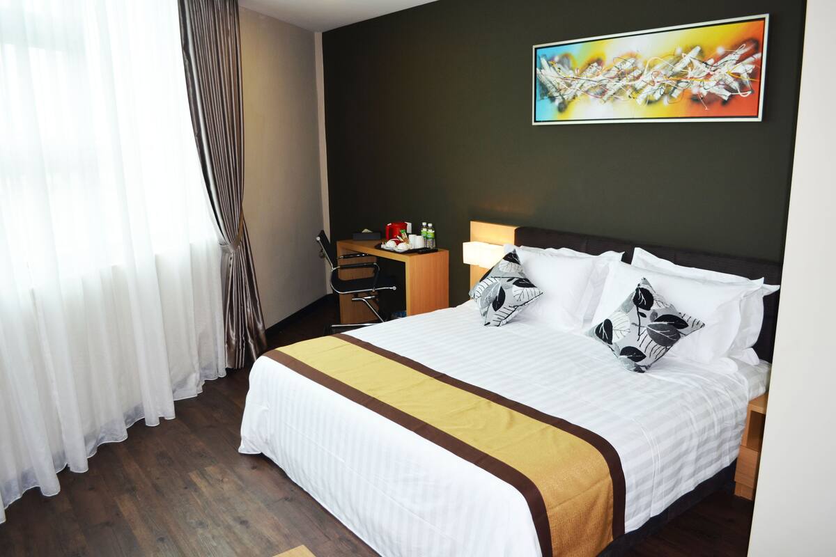A hotel room with a large bed, a desk, a chair, a lamp, and a painting on the wall.