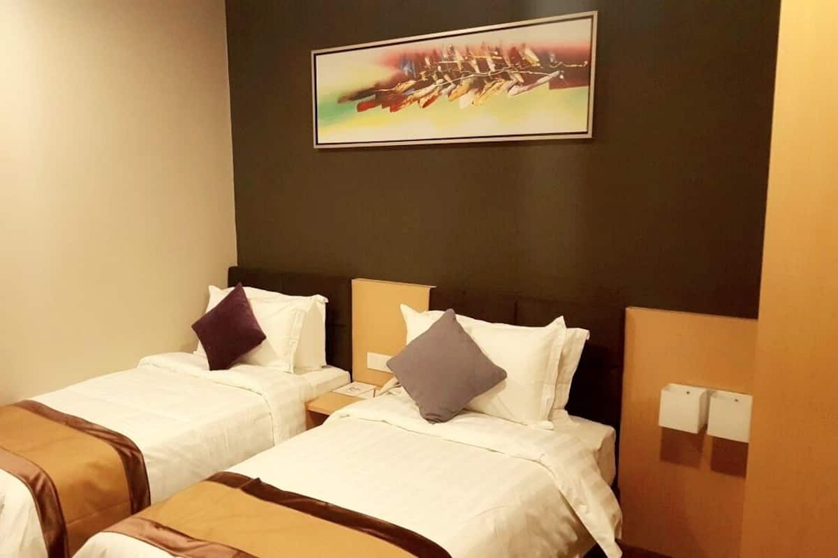 A hotel room with two beds, each with white linens and brown accents, a painting on the wall, and a nightstand with a lamp.