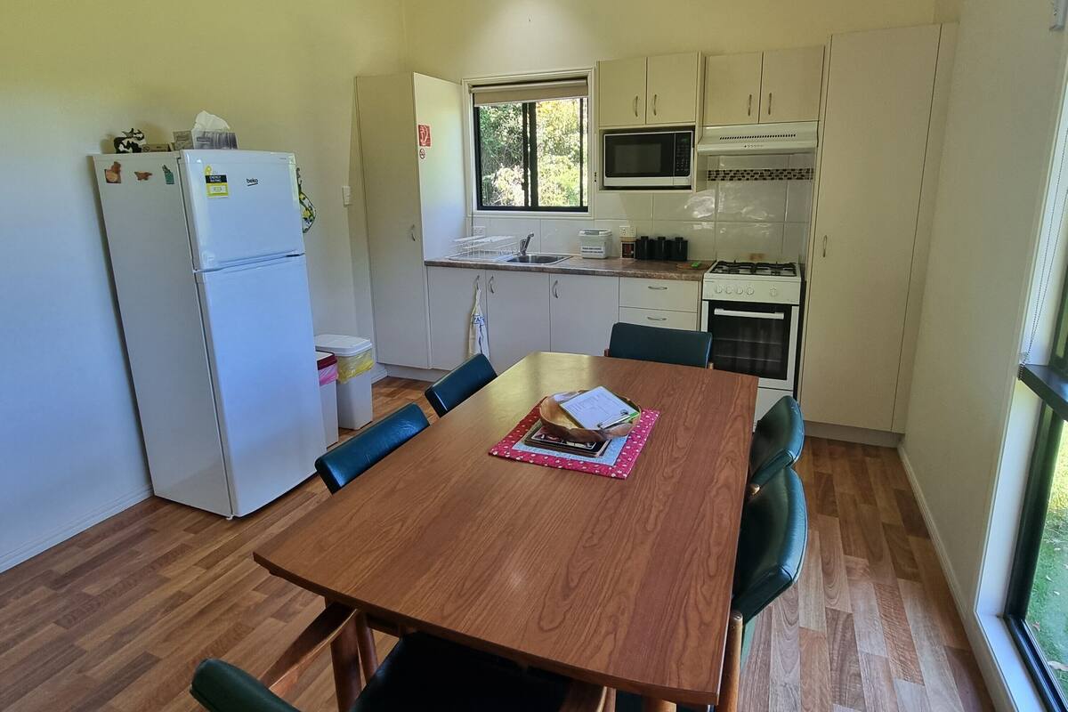 A compact kitchen with white cabinets, a microwave, a stove, and a refrigerator. There is a dining table with chairs and a window providing natural light.