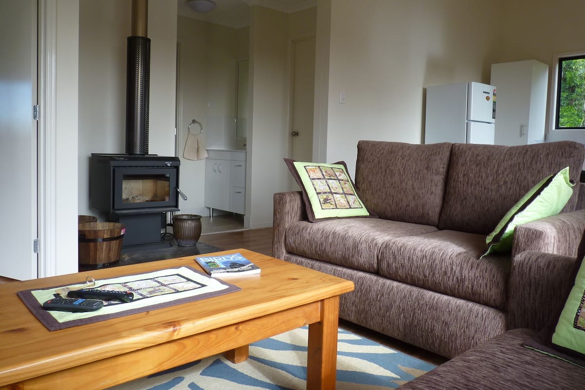 A living room with a sofa, a coffee table, a fireplace, and a kitchen area in the background.