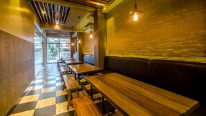 A restaurant interior with wooden benches and tables, a brick wall, and hanging pendant lights.