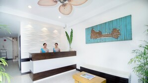 A reception area with a wooden reception desk, a bench, a wall-mounted artwork, and a ceiling fan.