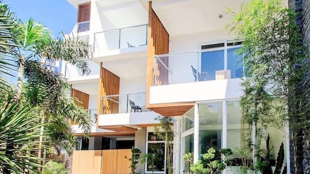 A modern multi-story building with a flat roof, large glass windows, and a wooden balcony.