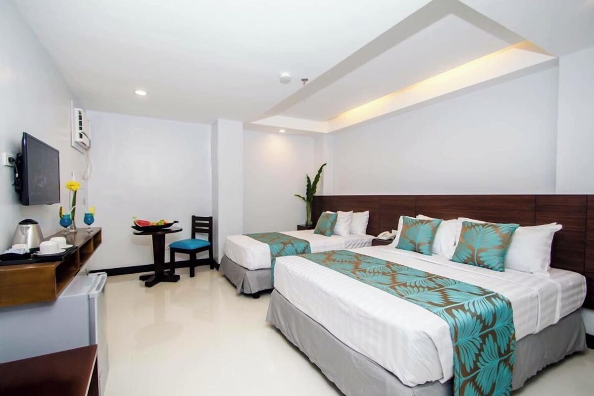 Quarto de hotel com duas camas, uma escrivaninha com computador, uma cadeira e uma mesinha de centro com uma fruteira.