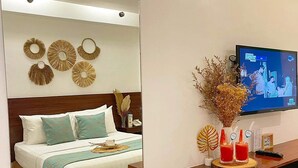 A modern hotel room with a large mirror reflecting the bed and decor, a flat-screen TV mounted on the wall, and a wooden console table with decorative items.