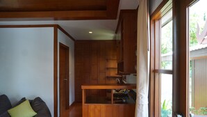 A modern kitchen with wooden cabinets and a small island, a black leather couch with a green pillow, and a door leading outside. - Kaya Mani Thai Villa Resort Samui (Koh Samui)