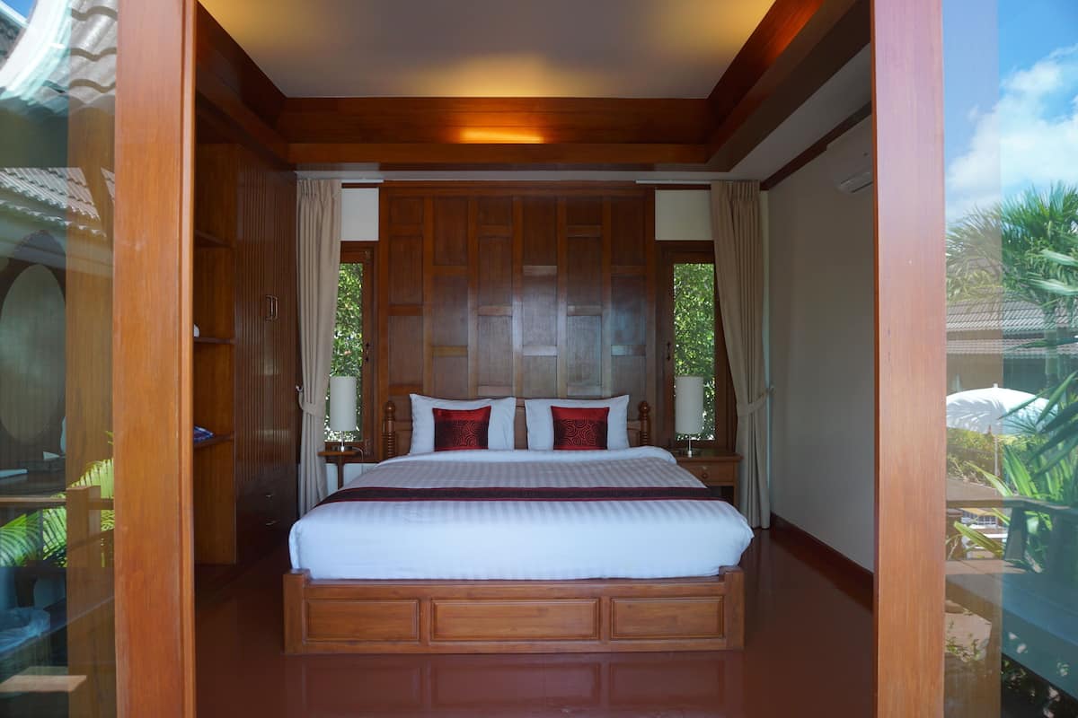 Quarto com estrutura de madeira, uma cama grande, cortinas e vista para o verde lá fora.