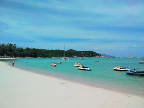 Une plage avec une eau turquoise et limpide, des bateaux et une personne qui se promène le long du rivage.