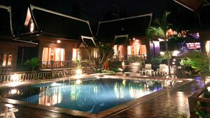 A nighttime view of a hotel with a swimming pool, wooden buildings, and outdoor seating areas. - Kaya Mani Thai Villa Resort Samui (Koh Samui)