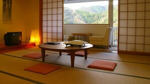 Une pièce avec un sol recouvert de tatamis, une petite table basse, des coussins, un téléviseur et une vue sur une forêt, visible à travers une porte coulissante.