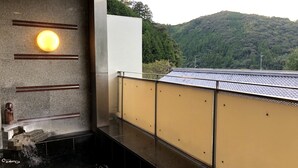 Un onsen japonais traditionnel, avec un bain en pierre, une statue en bois et une vue sur une montagne boisée.