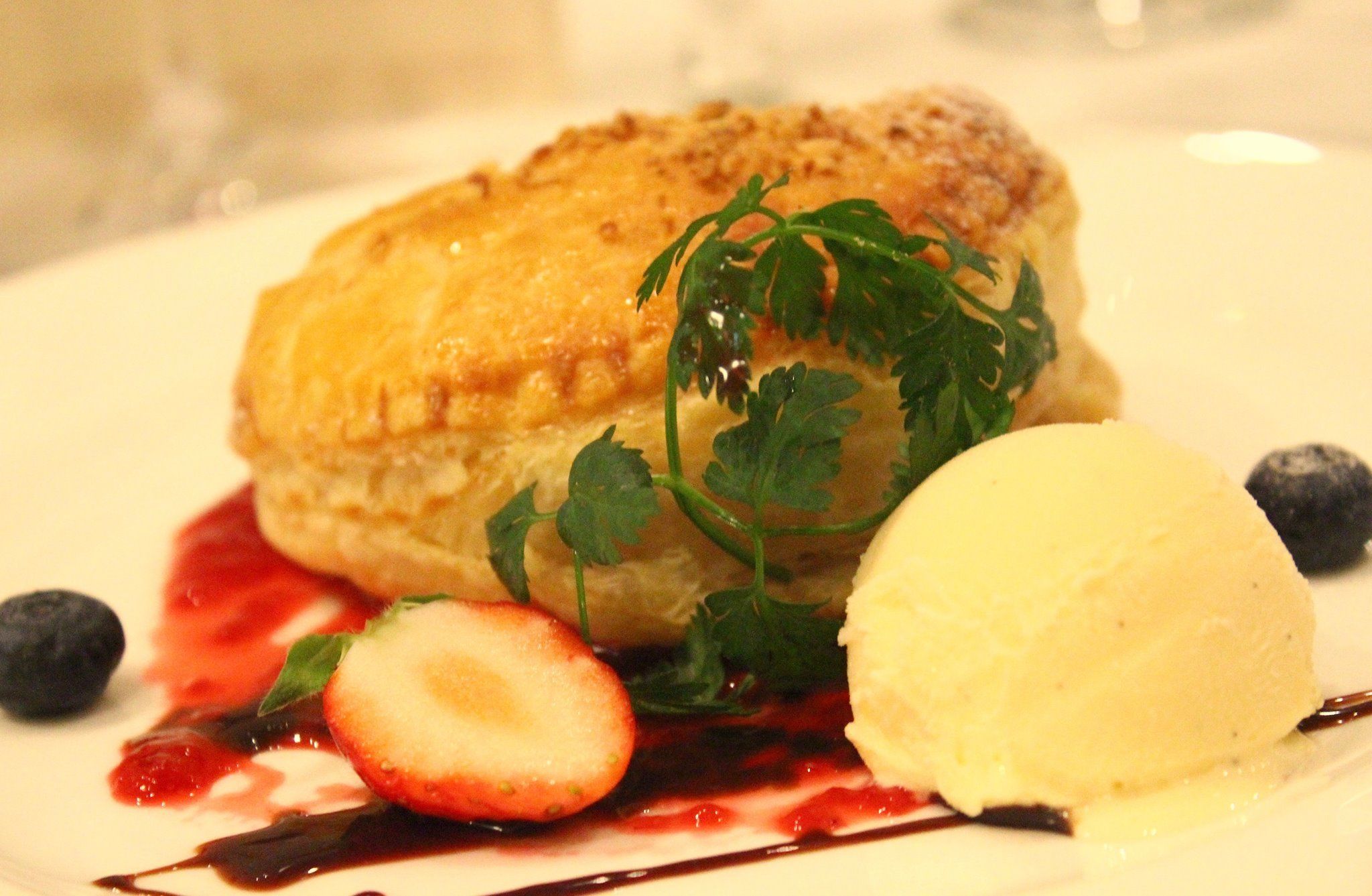 Une assiette à dessert avec une pâtisserie, des fraises, des myrtilles et une boule de glace.
