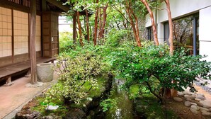 Un jardin japonais traditionnel, avec un ruisseau de pierres, des rochers couverts de mousse et un bâtiment en bois doté de portes coulissantes.