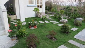 A well-maintained garden with a variety of potted plants and a stone pathway leading to a house with a white exterior and a blue archway. - GoodEatting (Jiaoxi)