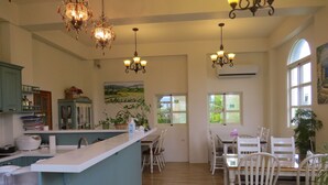 A spacious kitchen with a central island, wooden dining table, and chairs, surrounded by potted plants and a painting. - GoodEatting (Jiaoxi)