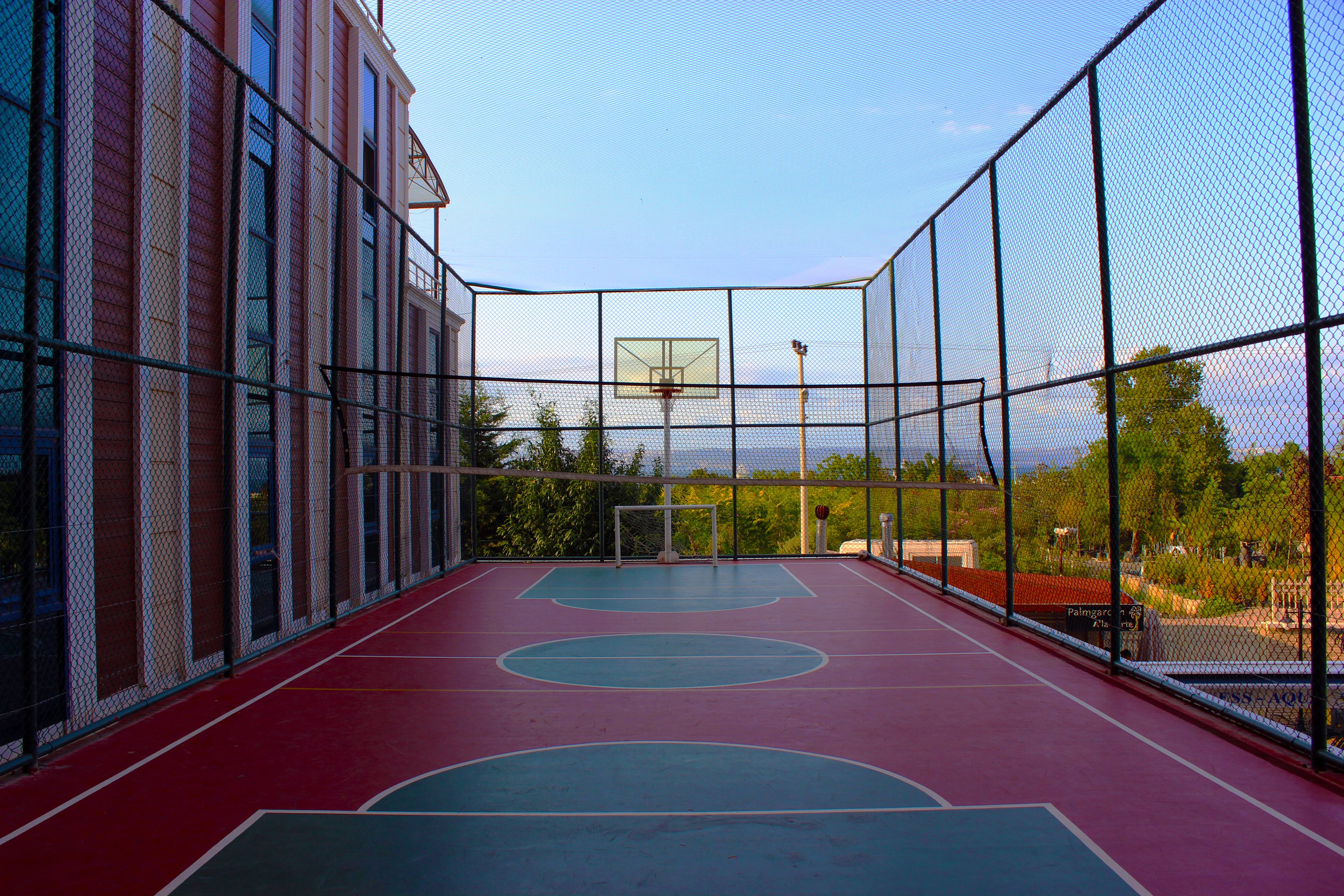 An outdoor basketball court with a net, a basketball hoop, and a red and blue floor.