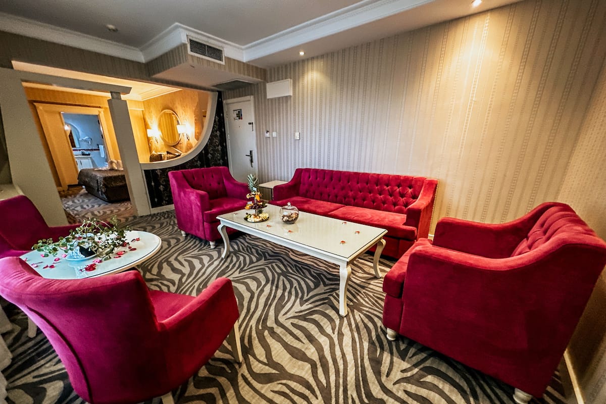 Une pièce avec un tapis à motifs zébrés, une table basse blanche et des fauteuils et un canapé recouverts d’un tissu rouge.