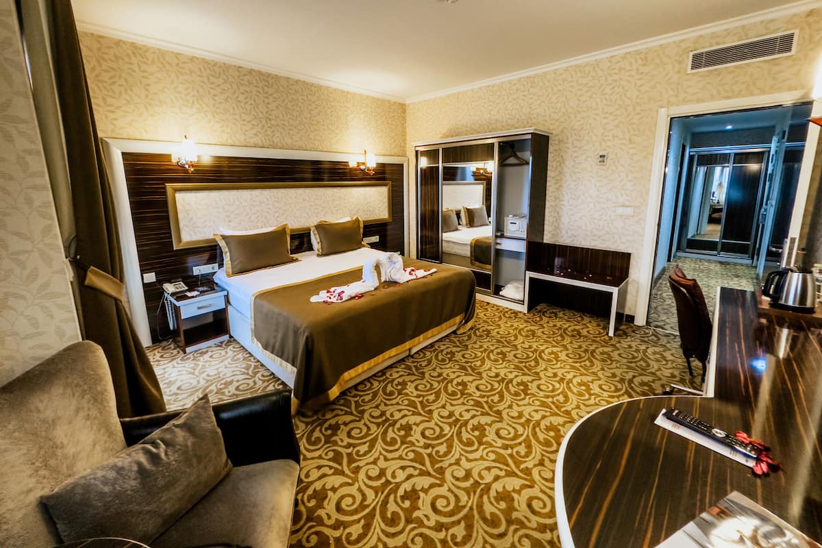 Une chambre d’hôtel avec un grand lit, un bureau, une chaise, une armoire et une salle de bain visible à travers une porte ouverte.