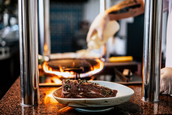 Un plat de viande agrémenté d’herbes, servi dans une assiette posée sur un comptoir, avec une structure métallique en arrière-plan.
