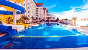 Una piscina con toboganes, un área de piscina con sillones de descanso, y un edificio de hotel con varios pisos y balcones.