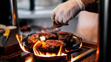Una persona asando filetes en una parrilla portátil con llamas.