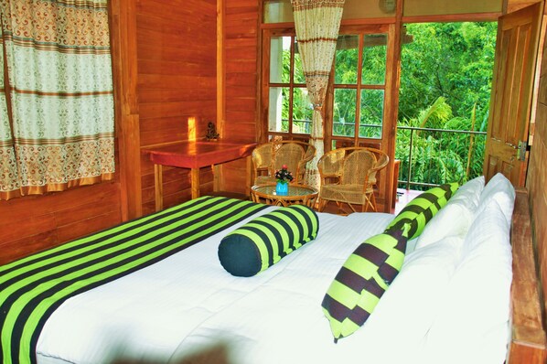 Una habitación de cabaña de madera con dos camas, una mesita y sillas cerca de una ventana que ofrece vistas a la vegetación.