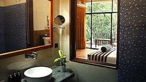 Une salle de bain avec un grand miroir, un lavabo et une plante en pot. On aperçoit un balcon avec une table et des chaises.