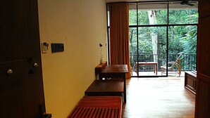 Une pièce avec un banc en bois, une petite table et une vue sur un balcon agrémenté de chaises et d’une balustrade.