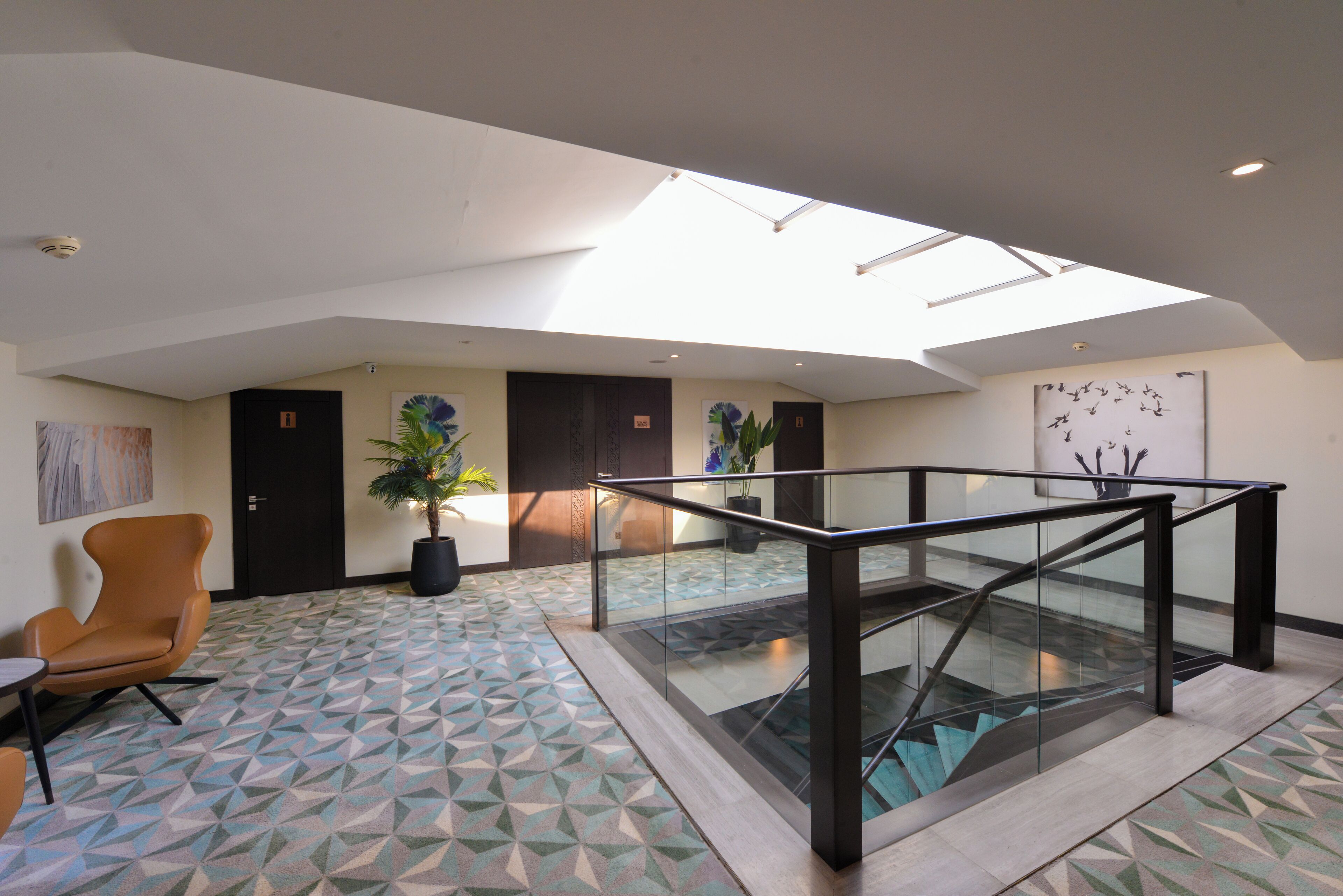 A spacious lobby with a geometric patterned floor, a glass staircase, and a skylight.