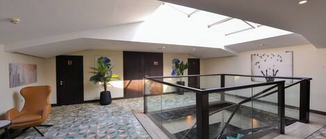 A spacious lobby with a geometric patterned floor, a glass staircase, and a skylight.
