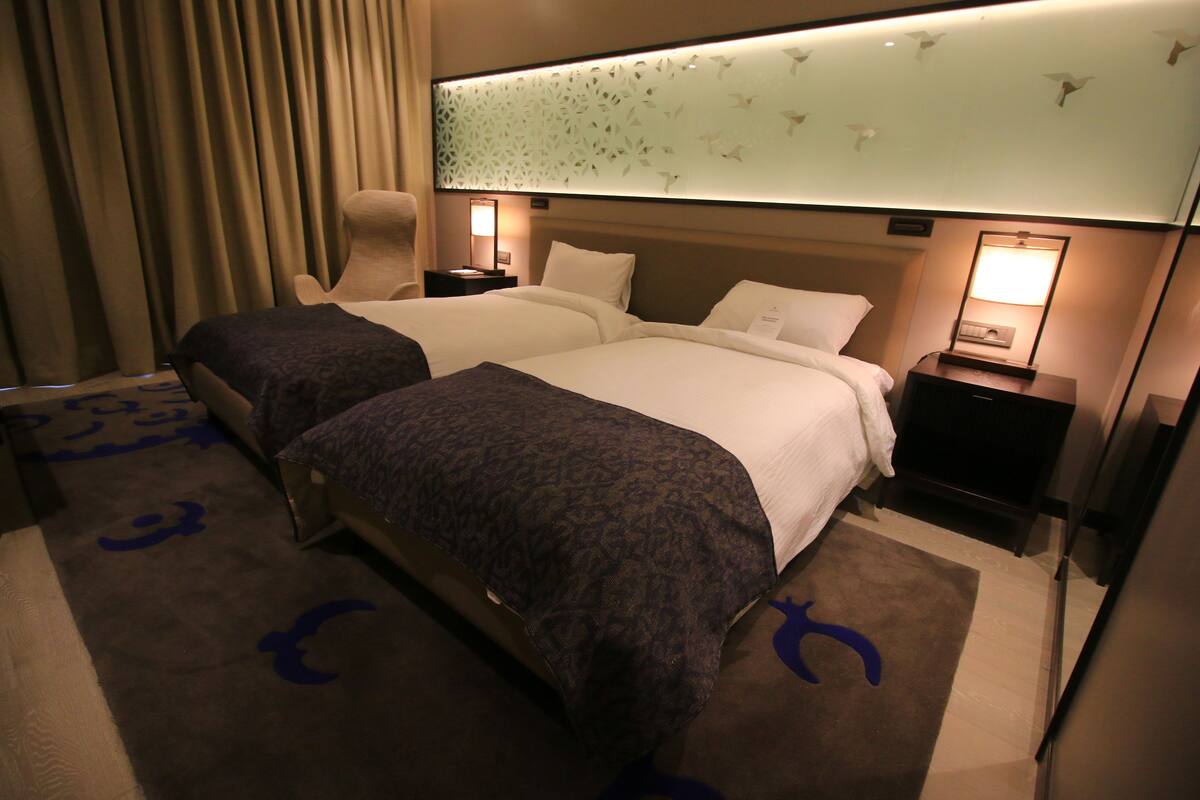 A hotel room with two beds, a large window with a view, and a desk with a lamp.