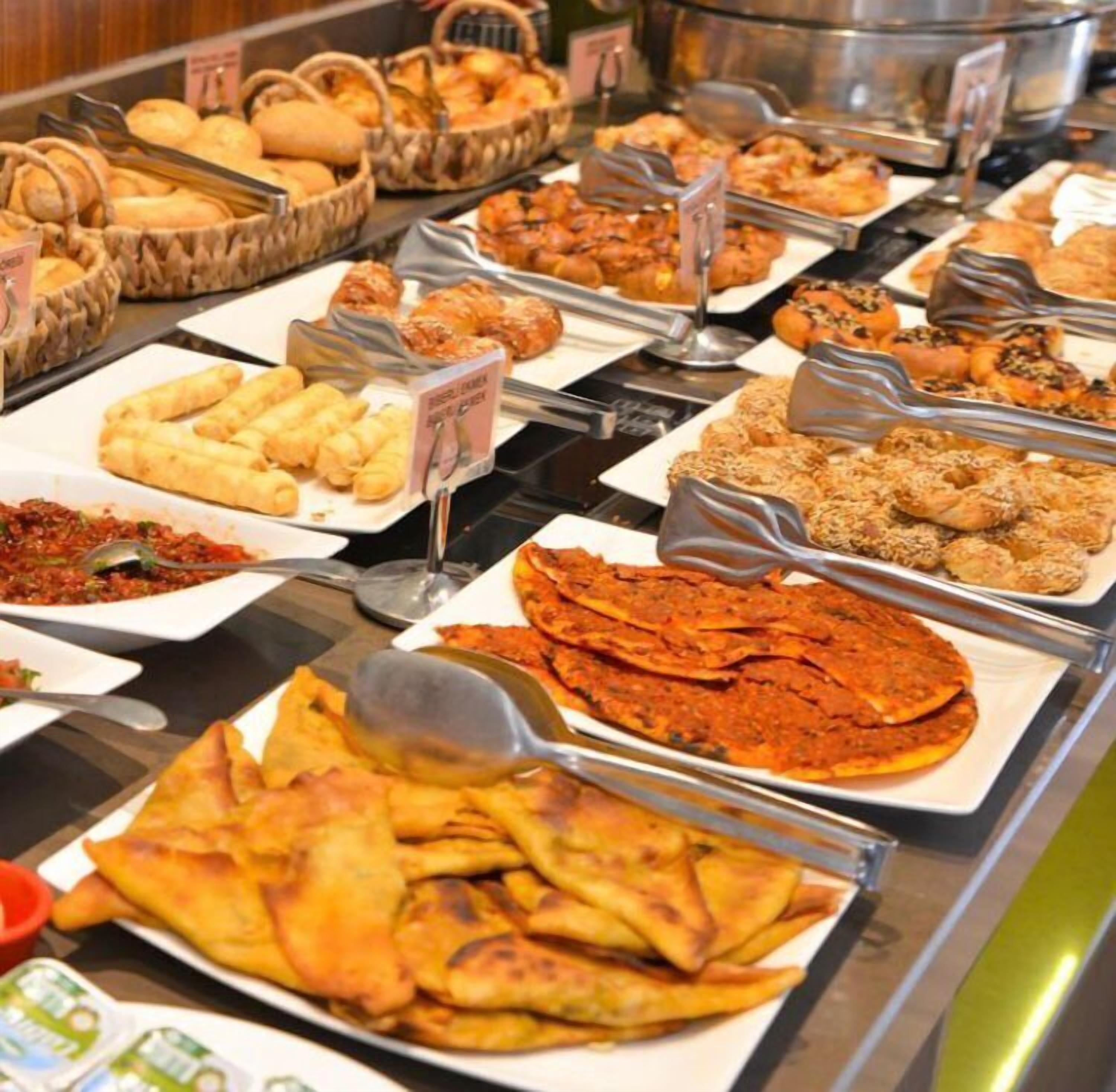 Un buffet proposant divers plats, notamment du pain, des pâtisseries et un grand plat de samoussas.