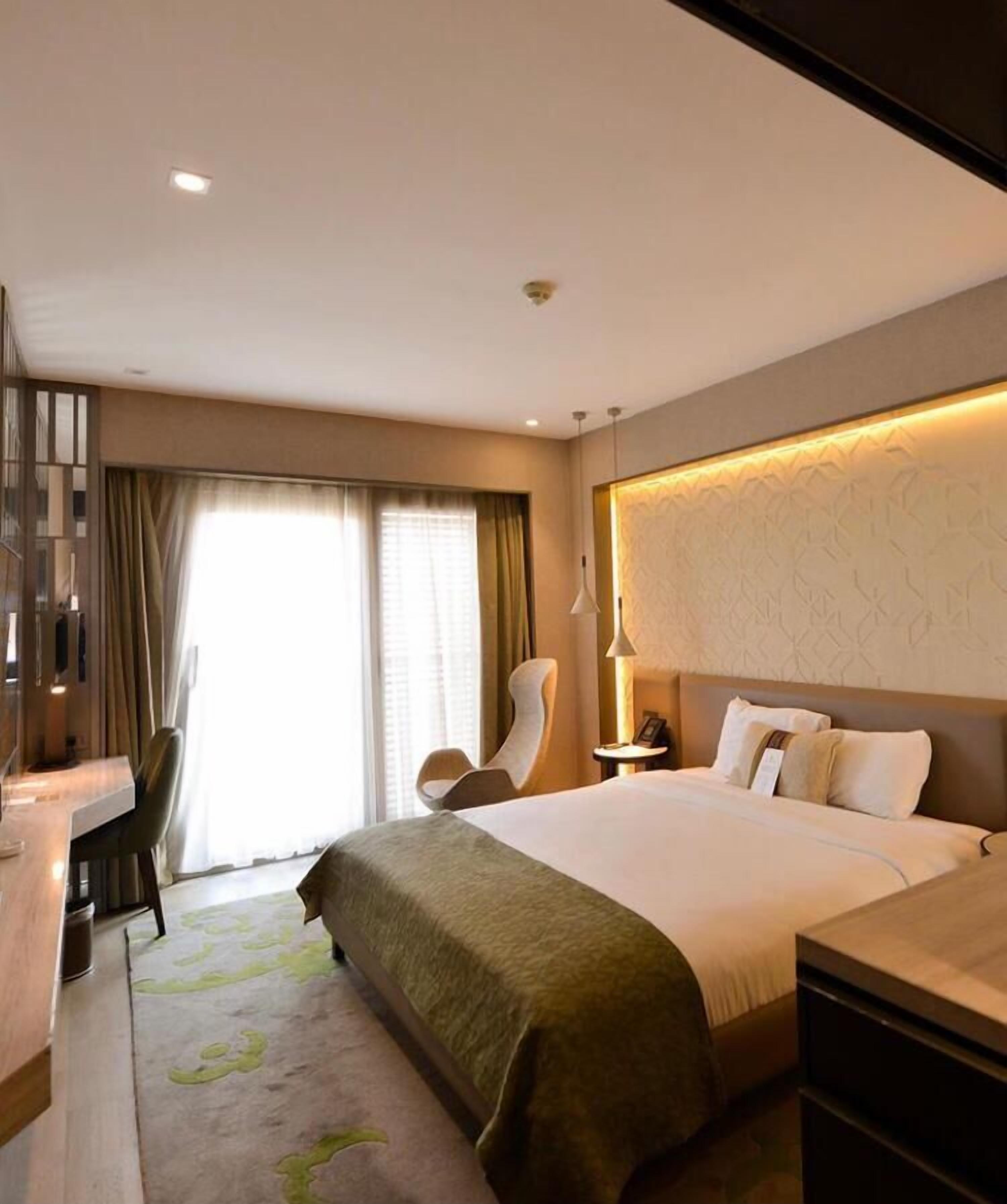 Habitación de hotel con una cama grande, un escritorio, una silla y vistas al exterior por la ventana.
