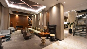A modern hotel lobby with a long reception desk, comfortable seating, a fireplace, and a staircase. - Waxwing Hotel (Antakya)
