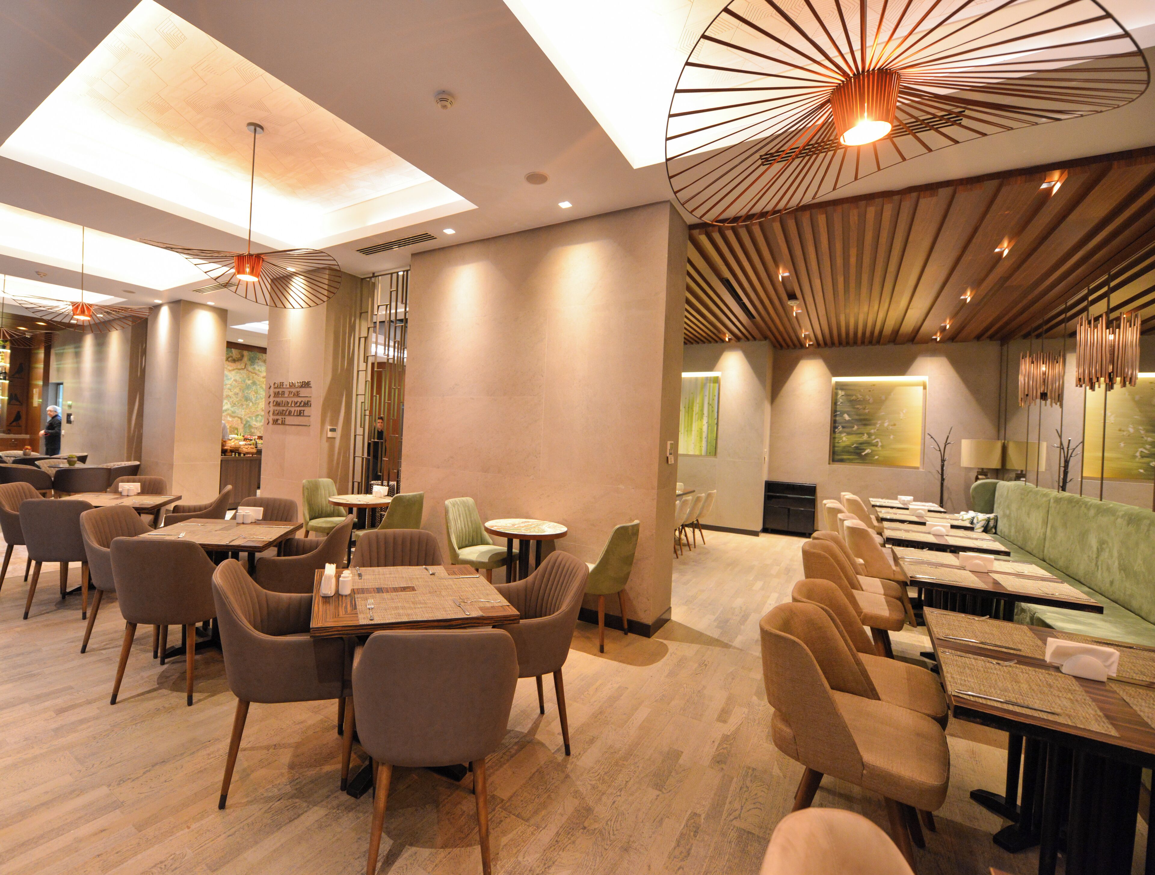 Um restaurante moderno com pé-direito alto, iluminação pendente e uma variedade de assentos, incluindo mesas e cabines.