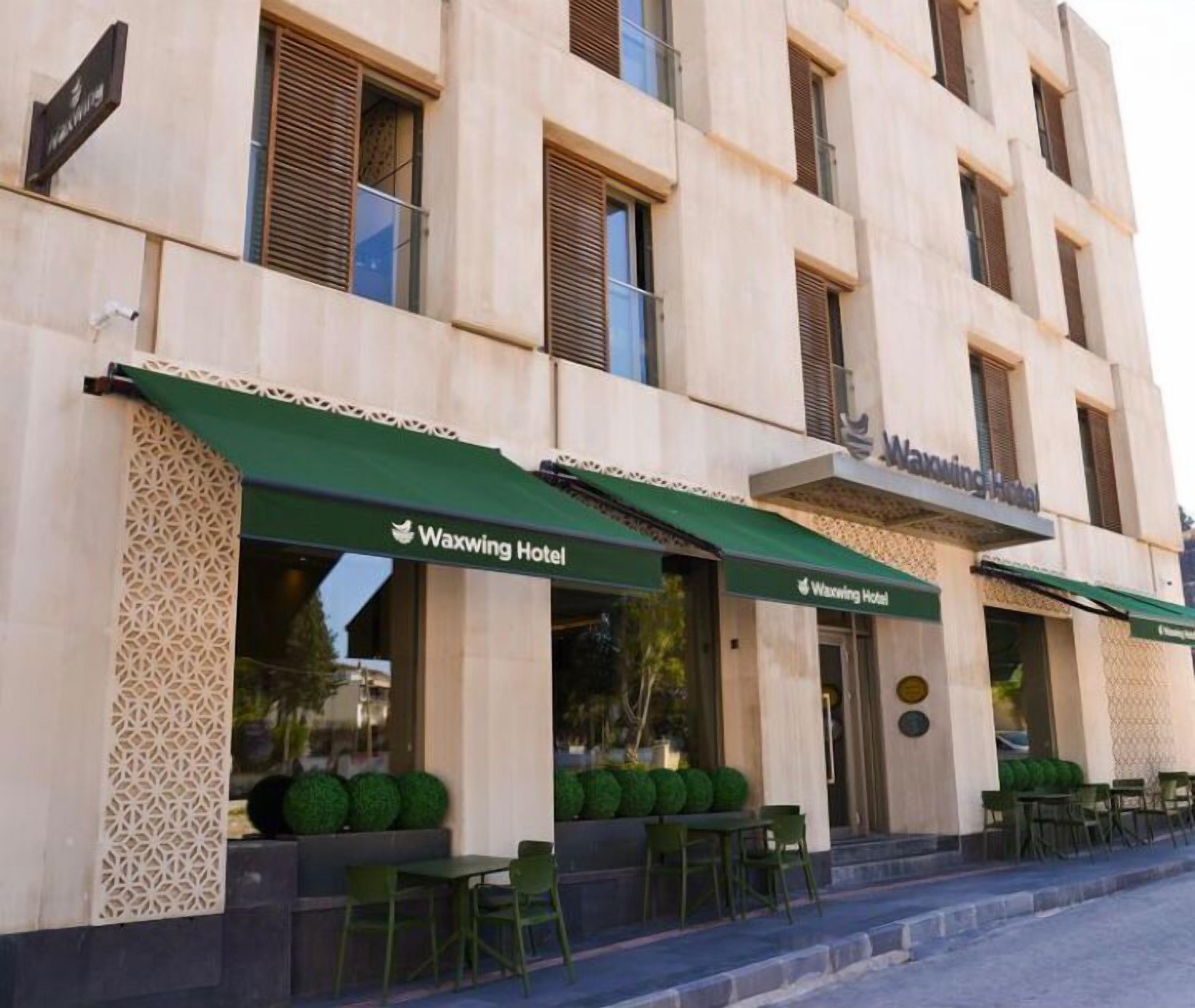 A building with multiple windows and a green awning labeled "Waxwing Hotel".