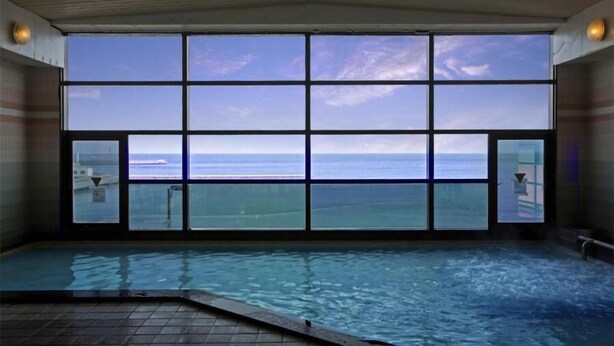 Una piscina interior con un ventanal grande que ofrece vista al océano.