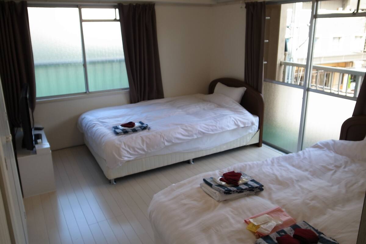 A hotel room with two beds, a window with curtains, an air conditioning unit, and a view of the sea.
