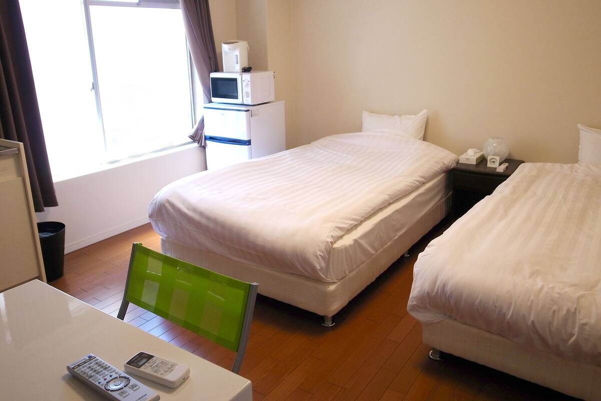 A hotel room with two beds, a desk, a chair, a microwave, and a small table with a telephone and a remote control.