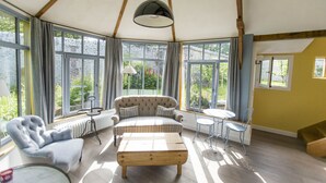 A spacious room with a large window, a sofa, a wooden coffee table, and a small round table with chairs. - Le Clos de Grâce (Honfleur)