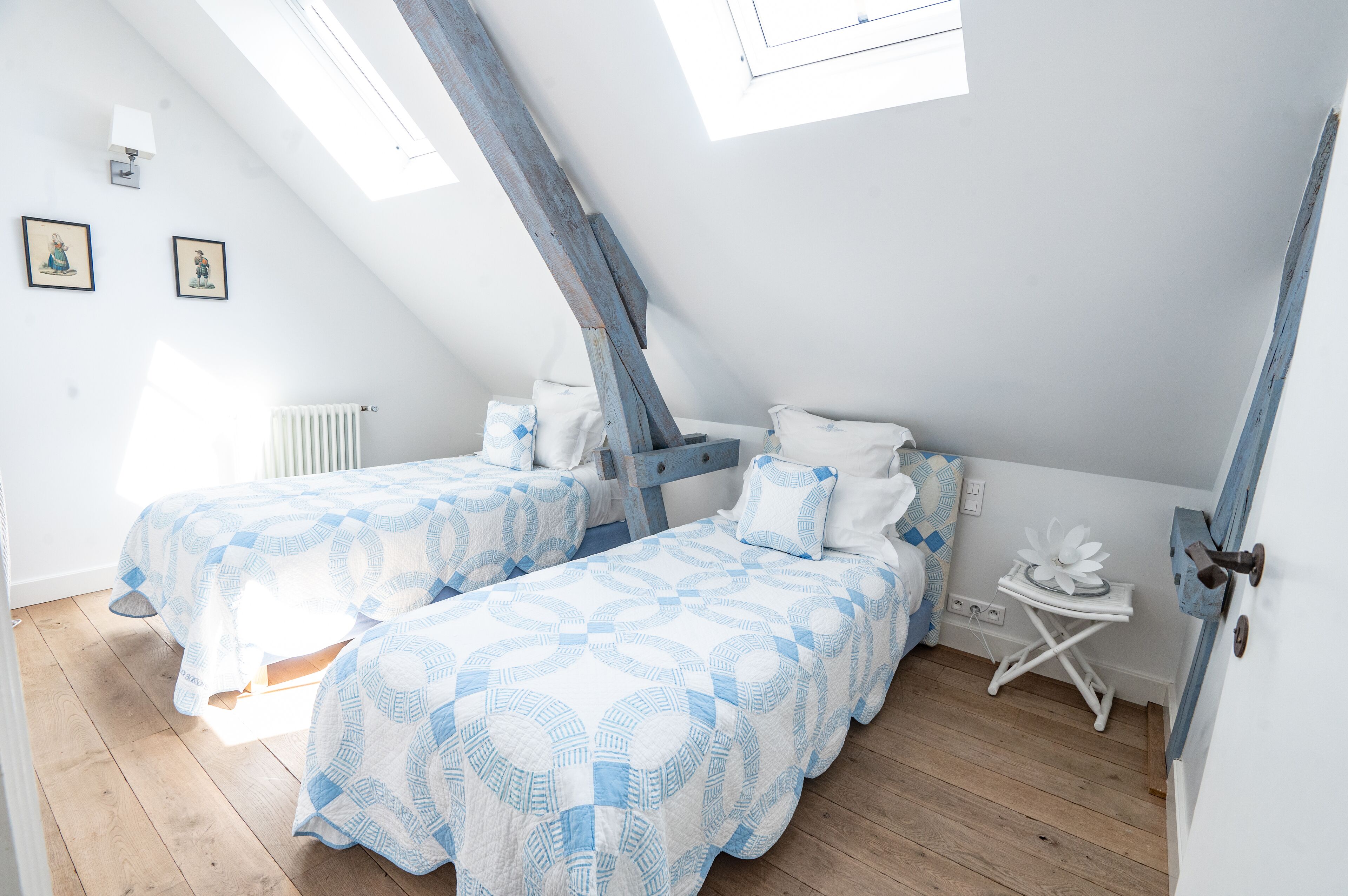 A room with two beds, a skylight, a radiator, and a small table with a decorative item.