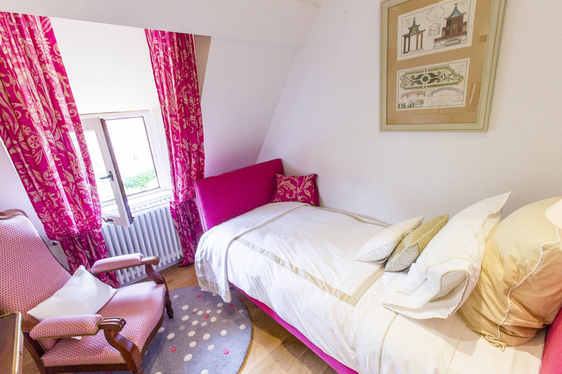 A bedroom with a bed, a chair, a window with curtains, and a radiator.