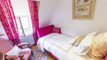A bedroom with a bed, a chair, a window with curtains, and a radiator.
