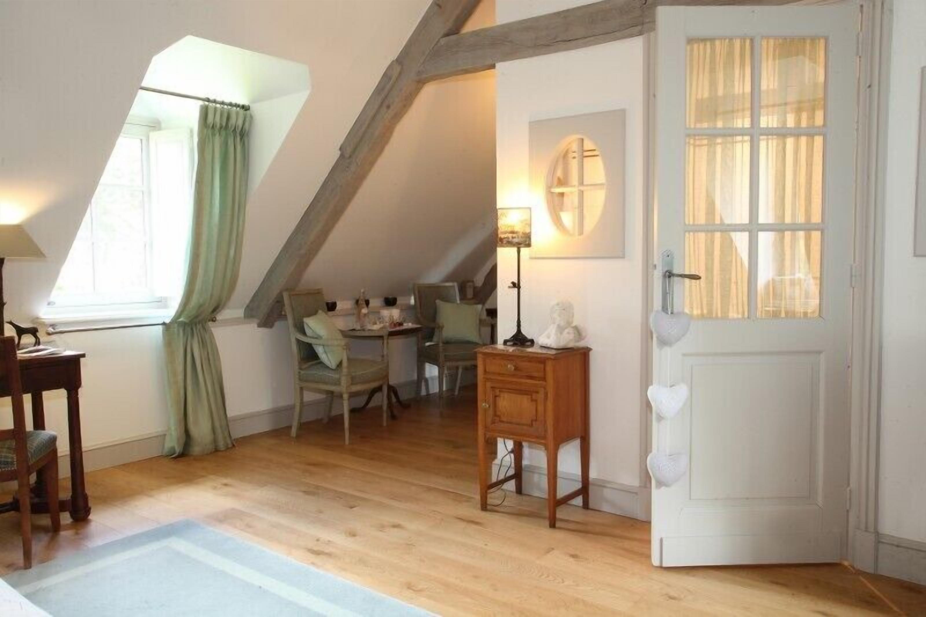 A cozy attic room with a sloped ceiling, wooden flooring, a dining area with chairs, a small table, and a white door with a window.