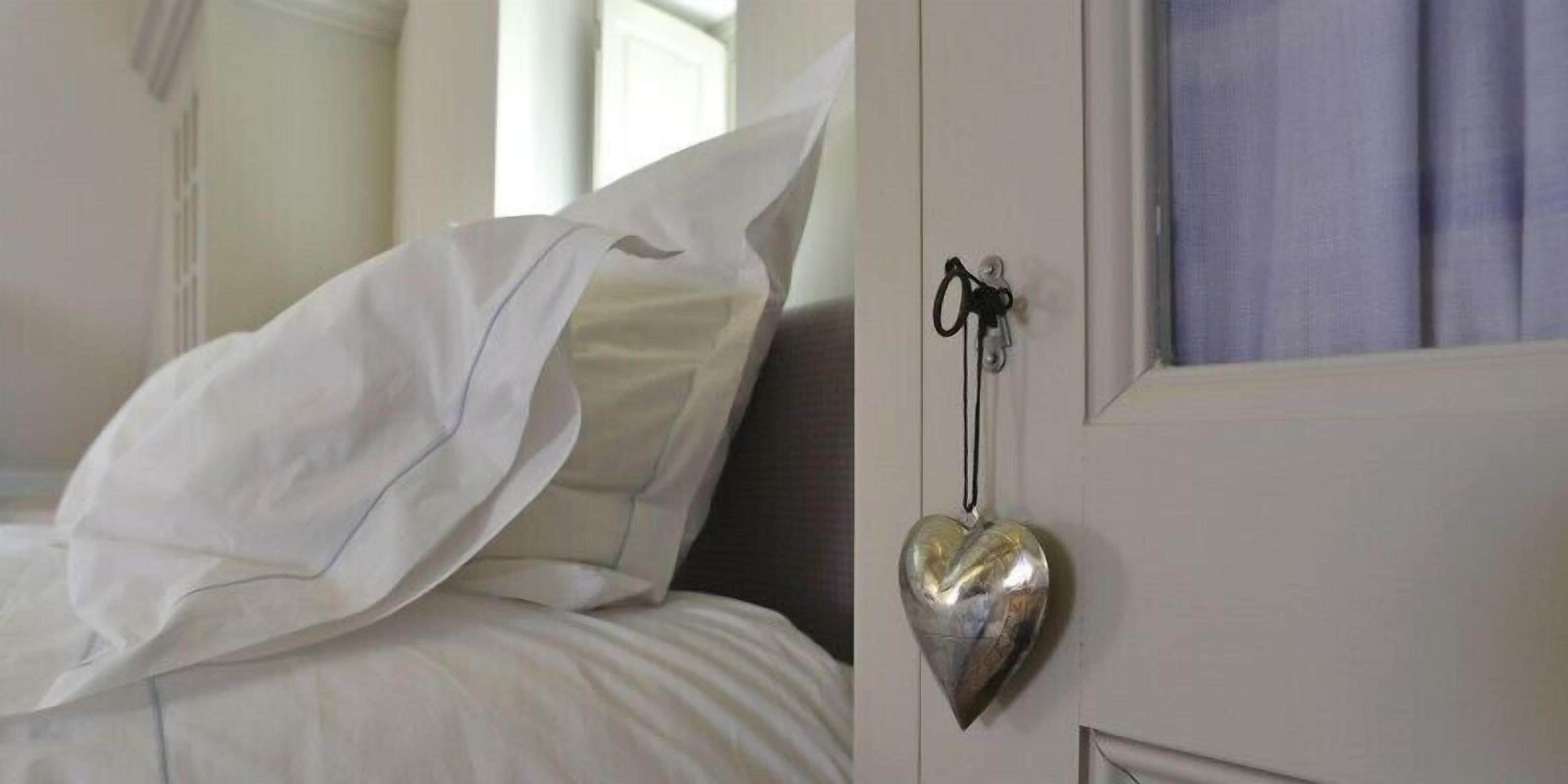 A bedroom with a bed, white bedding, and a heart-shaped keychain hanging on the door.