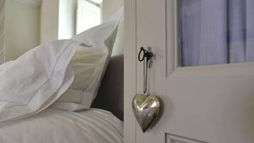A bedroom with a bed, white bedding, and a heart-shaped keychain hanging on the door.