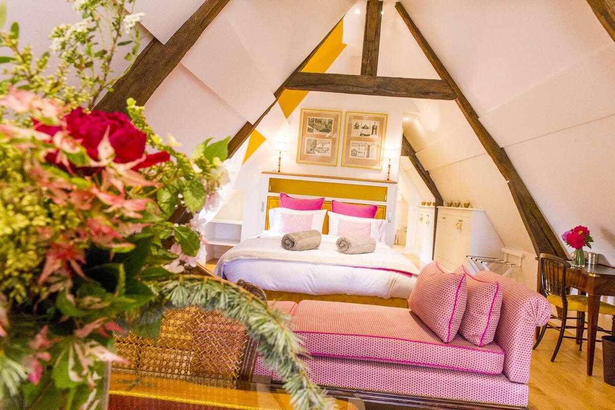 Um quarto tipo tenda aconchegante, triangular, com uma cama, um sofá e uma mesa pequena.