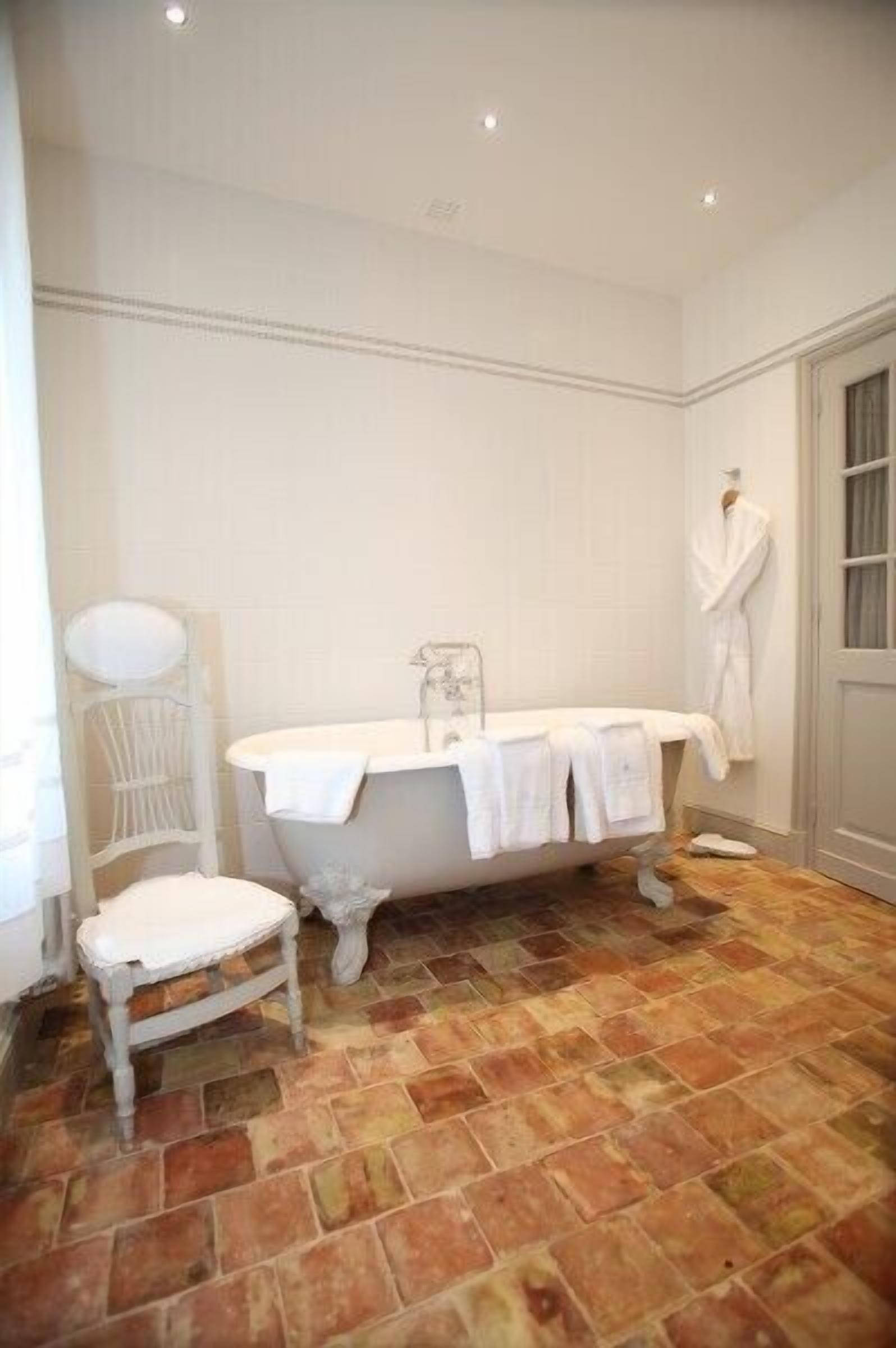Ein Badezimmer mit einer freistehenden Badewanne, einem weißen Stuhl und einem weißen Bademantel, der an der Wand hängt.