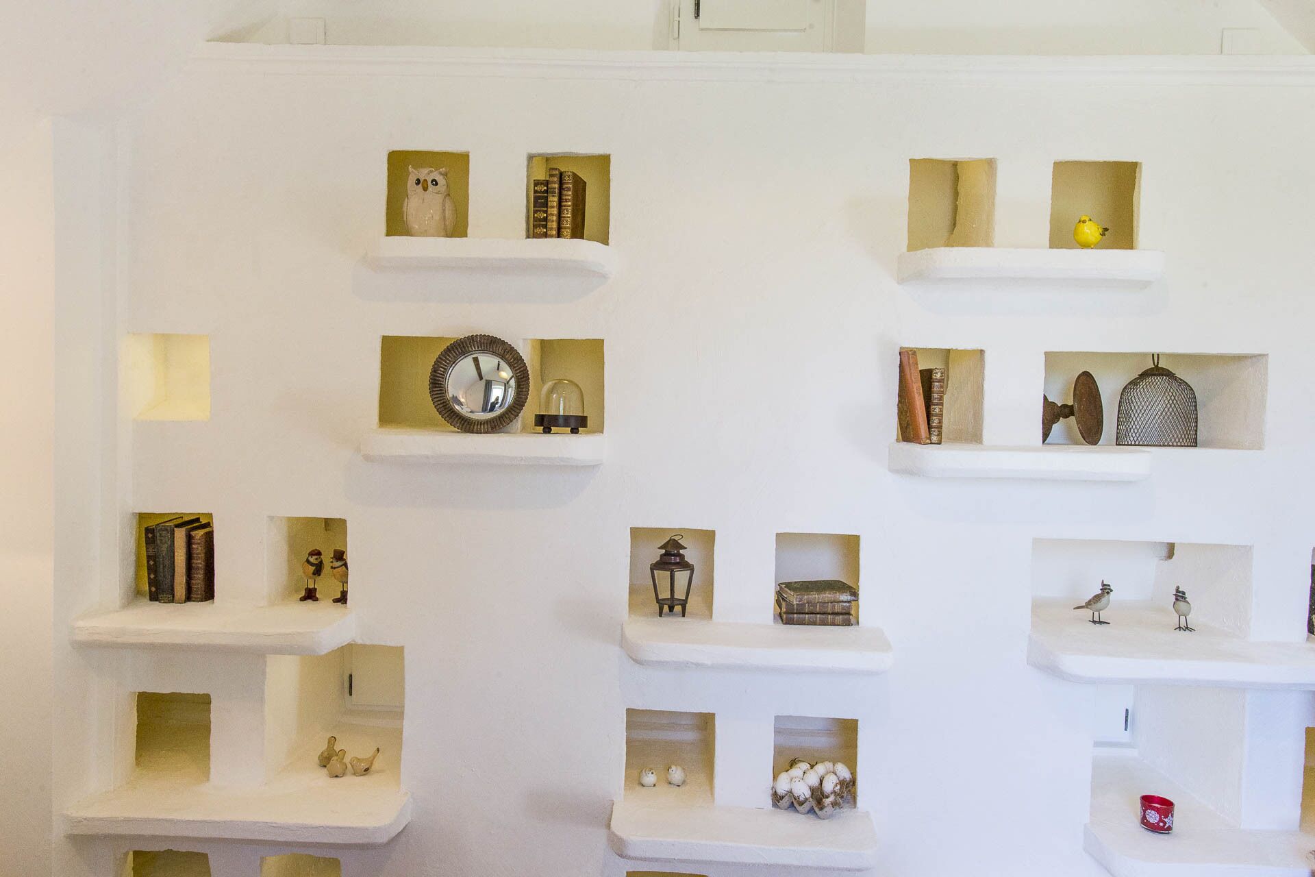 A wall with multiple white shelves displaying various decorative items.